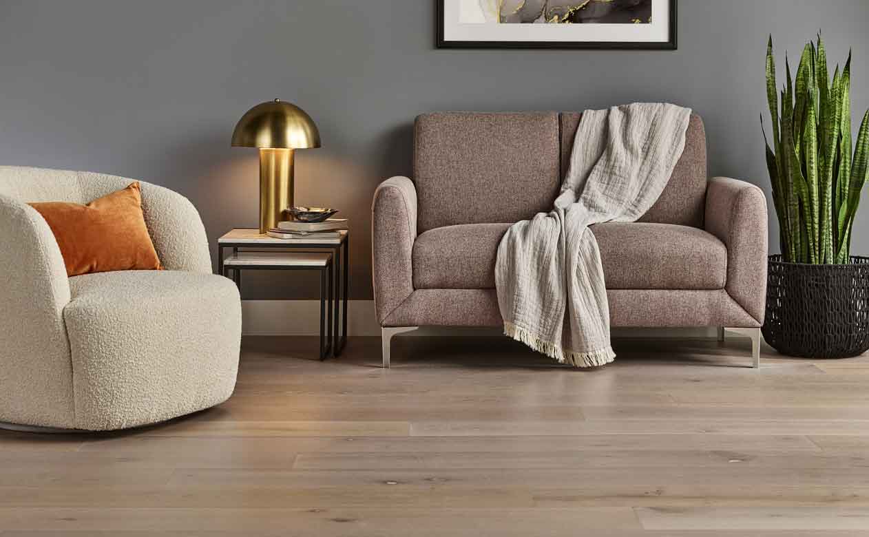 mid-toned hardwood flooring in living room with boucle chair and beige couch